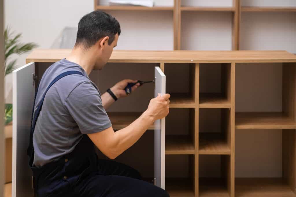 Custom furniture delivery and assembly master attaching white door to wooden cabinet