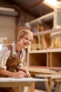 Female Apprentice Working As Carpenter In Furniture Workshop