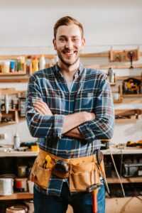 happy carpenter in apron standing with crossed arms